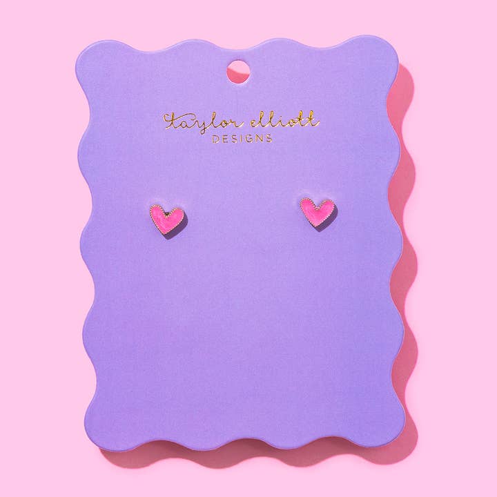 Pink heart stud earrings displayed on a purple scalloped backer card with Taylor Elliot Designs branding.