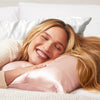 Model resting on a blush satin pillowcase while smiling