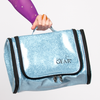 Light blue hanging cosmetics bag shown open with compartments visible and a hand holding the top strap.