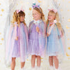 Three young girls wearing matching pastel unicorn-themed tulle capes and matching headbands, standing together in a decorated studio with silver curtains and gold star and moon decorations.