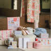 Collection of items including mugs, boxes, and a hat on a surface with a floral curtain in the background.