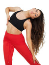 Dancer wearing a black racerback bra top and red dance pants stretching to the side