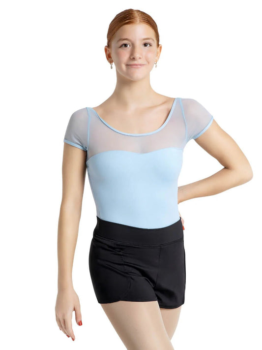 Young dancer wearing black dance shorts with a light blue leotard standing against a white background