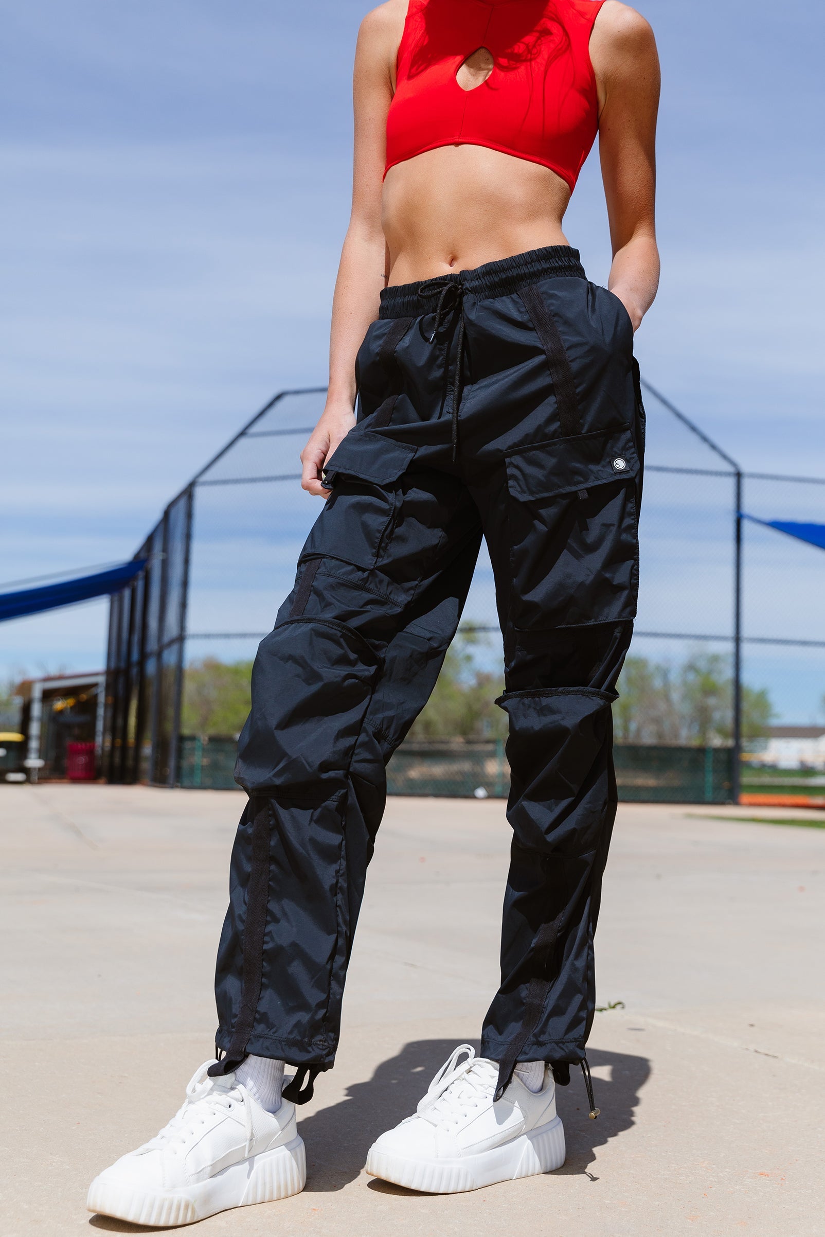 Adult dancer wearing black cargo-style dance pants, standing outdoors with hands on hips.