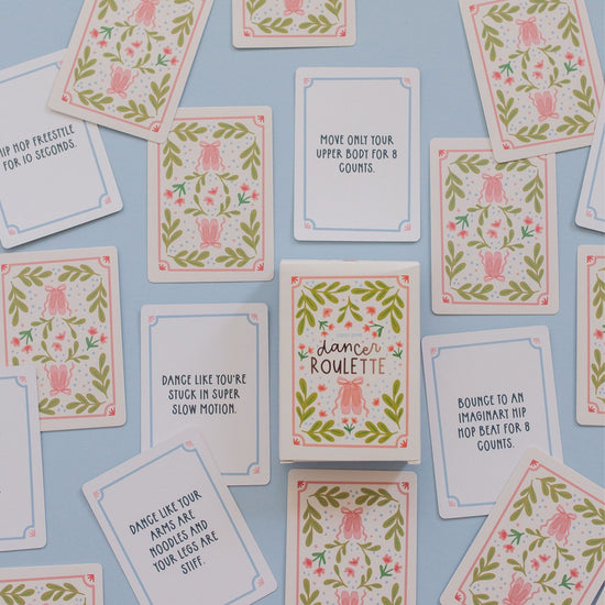 A flat-lay arrangement of square dance cards with pink and green floral borders and various dance-related phrases, displayed on a light blue background.