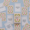 A flat-lay arrangement of square dance cards with pink and green floral borders and various dance-related phrases, displayed on a light blue background.