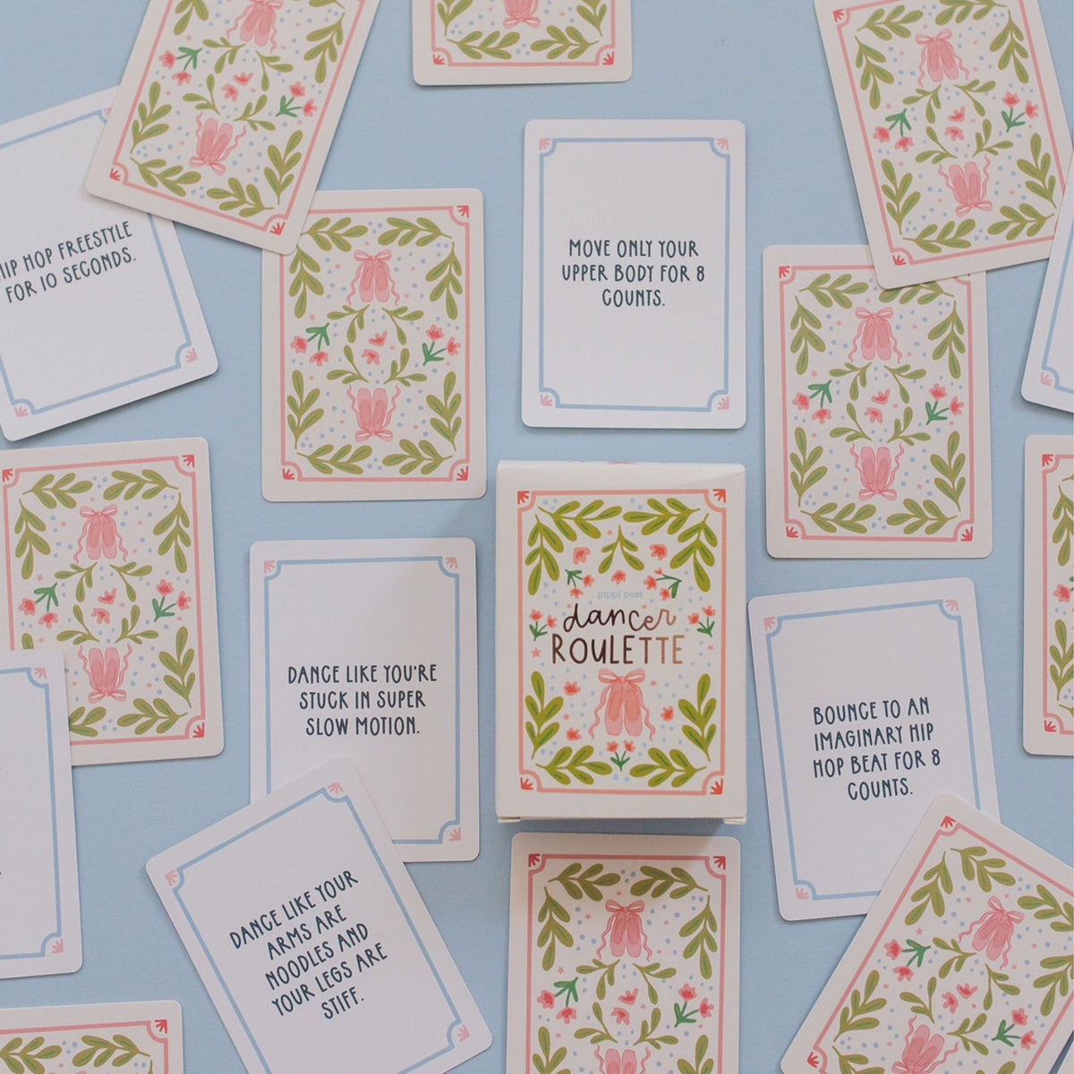 A flat-lay arrangement of square dance cards with pink and green floral borders and various dance-related phrases, displayed on a light blue background.