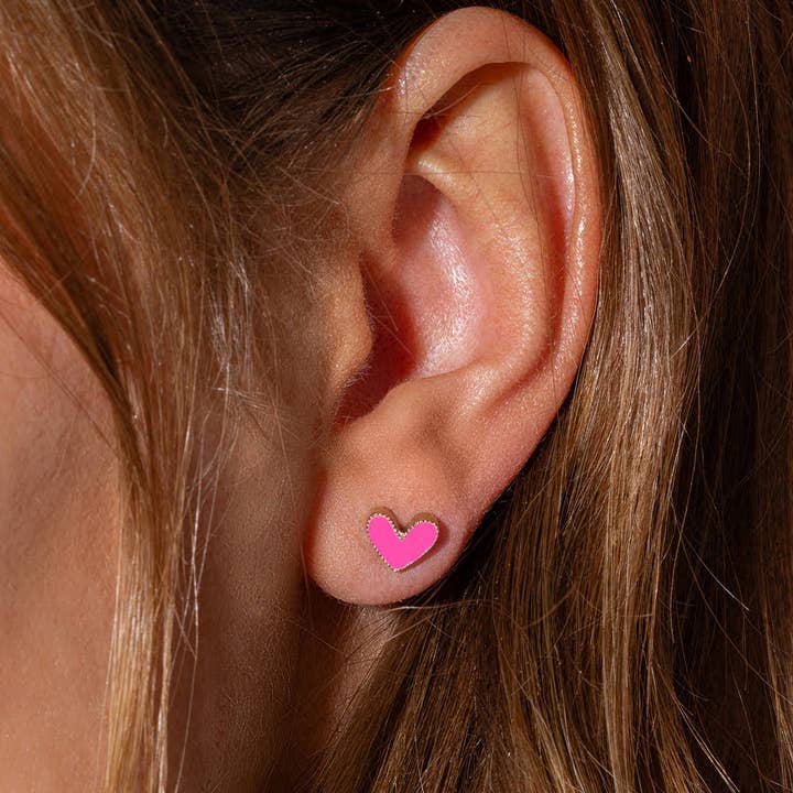 Close-up of a pink heart stud earring worn in an ear.