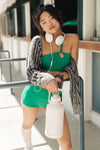 Adult dancer wearing a green dance bra with coordinating bottoms, standing outdoors near steps.