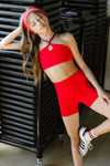 Adult dancer wearing a red dance bra with matching bottoms, standing near a wall.