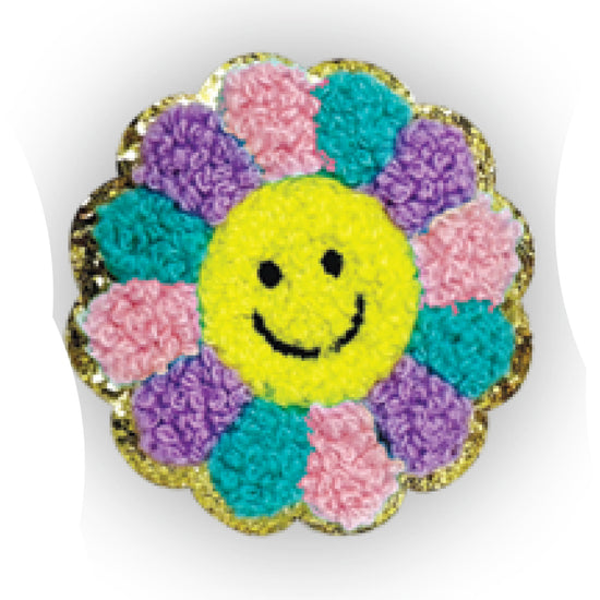 A round embroidered patch shaped like a flower with a yellow smiley face in the center and multicolored textured petals in pink, purple, and teal, outlined with a gold glittery border on a white background.