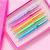 Five colorful pens laid diagonally on a pink surface, showing different pen colors and designs.
