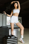 Adult dancer wearing white dance shorts with a matching top, posing indoors.