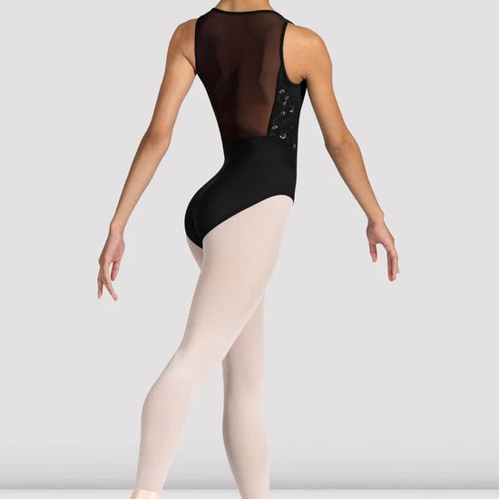 Back view of dancer wearing a black leotard with mesh back detail walking in ballet shoes and tights